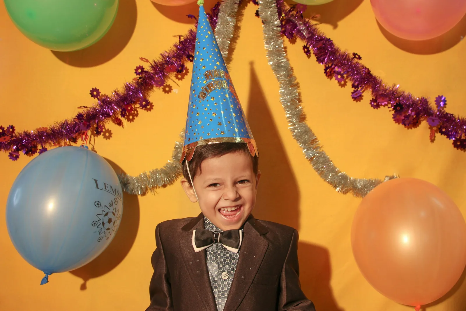 Smiling boy in a party hat in front of balloons and tinsel at a kids' birthday party